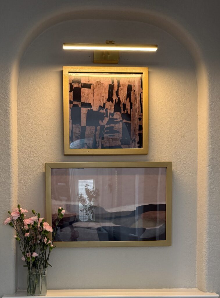 After photo of a decorated arched wall niche with stacked gold-framed art and a brass picture light