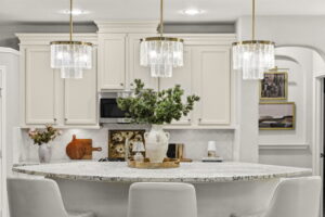 Custom off-white kitchen cabinets and stone island styled with brass pendant lights in a Houston, Texas home