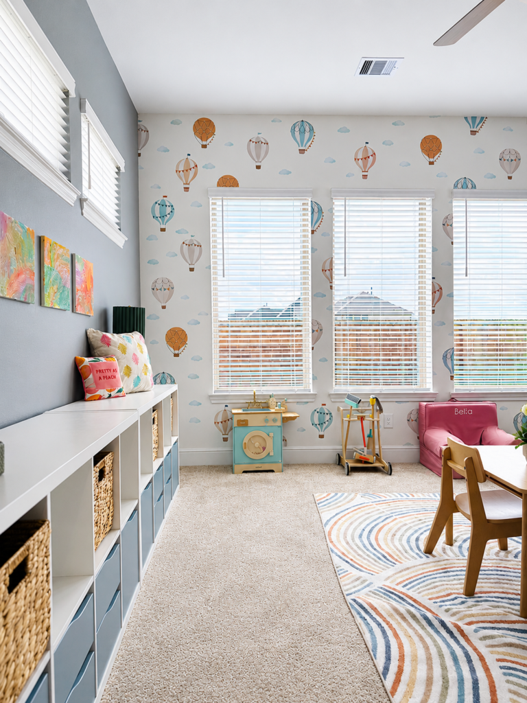 Low-profile white toy storage shelves and hot air balloon wallpaper inside a childrens playroom refresh in Cypress, TX.