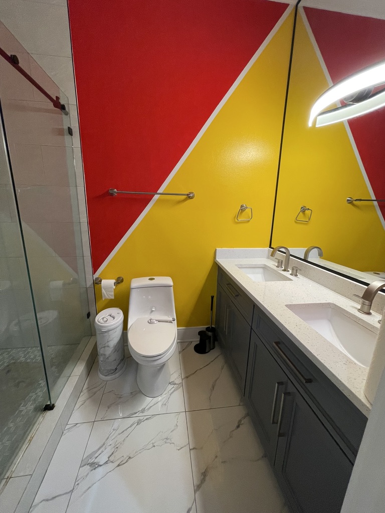 Before photo of a bathroom in The Woodlands, TX with bold red and yellow painted geometric walls and a dark gray vanity.