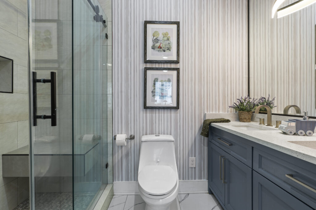 After photo of a simple bathroom makeover in Houston, TX featuring striped wallpaper, stacked framed art, a bath mat, and vanity decor.
